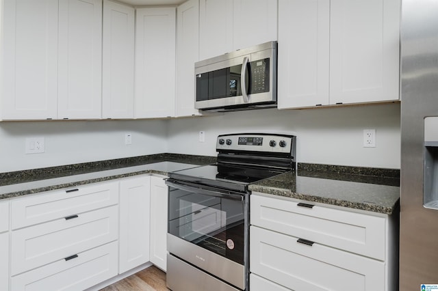 kitchen featuring light hardwood / wood-style floors, white cabinets, appliances with stainless steel finishes, and dark stone countertops