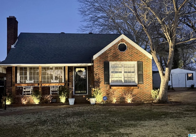 view of front of house with a front yard, covered porch, and a storage shed