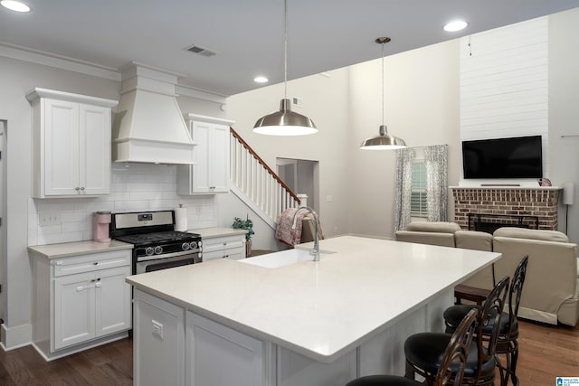 kitchen with backsplash, pendant lighting, sink, stainless steel range with gas stovetop, and custom range hood