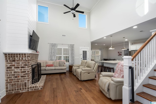 living room featuring a high ceiling, a fireplace, ceiling fan, hardwood / wood-style flooring, and crown molding