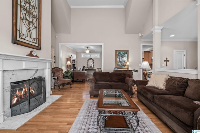 living room featuring a premium fireplace, ceiling fan, decorative columns, ornamental molding, and light wood-type flooring