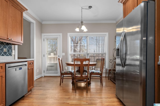 kitchen with appliances with stainless steel finishes, an inviting chandelier, hanging light fixtures, tasteful backsplash, and light wood-type flooring