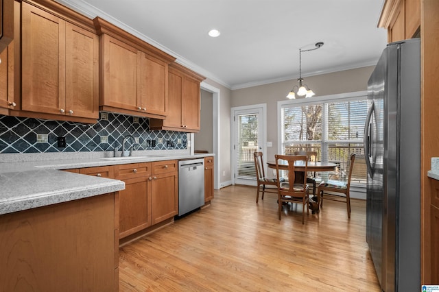 kitchen with appliances with stainless steel finishes, decorative light fixtures, sink, ornamental molding, and light hardwood / wood-style flooring