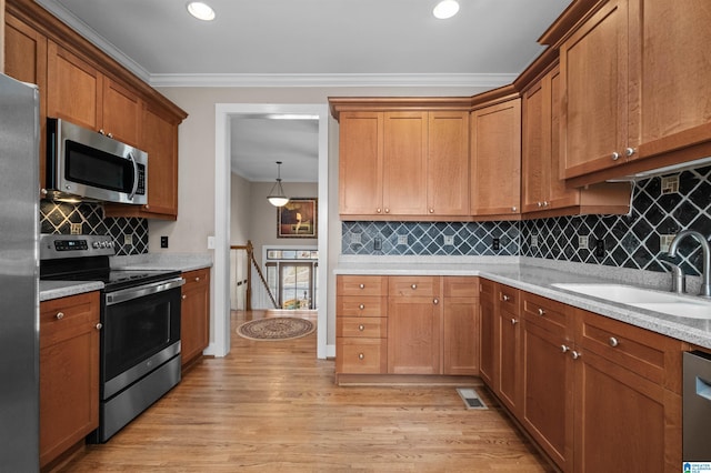 kitchen featuring sink, crown molding, appliances with stainless steel finishes, light stone countertops, and light hardwood / wood-style floors