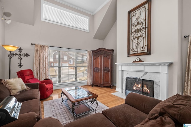 living room featuring a towering ceiling, a premium fireplace, ornamental molding, and light hardwood / wood-style flooring