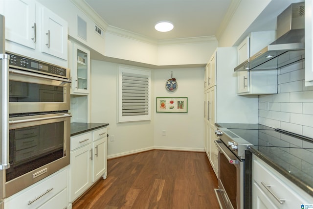 kitchen with appliances with stainless steel finishes, wall chimney exhaust hood, tasteful backsplash, white cabinetry, and ornamental molding