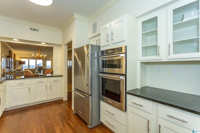 kitchen with appliances with stainless steel finishes, white cabinets, dark hardwood / wood-style floors, dark stone countertops, and an inviting chandelier