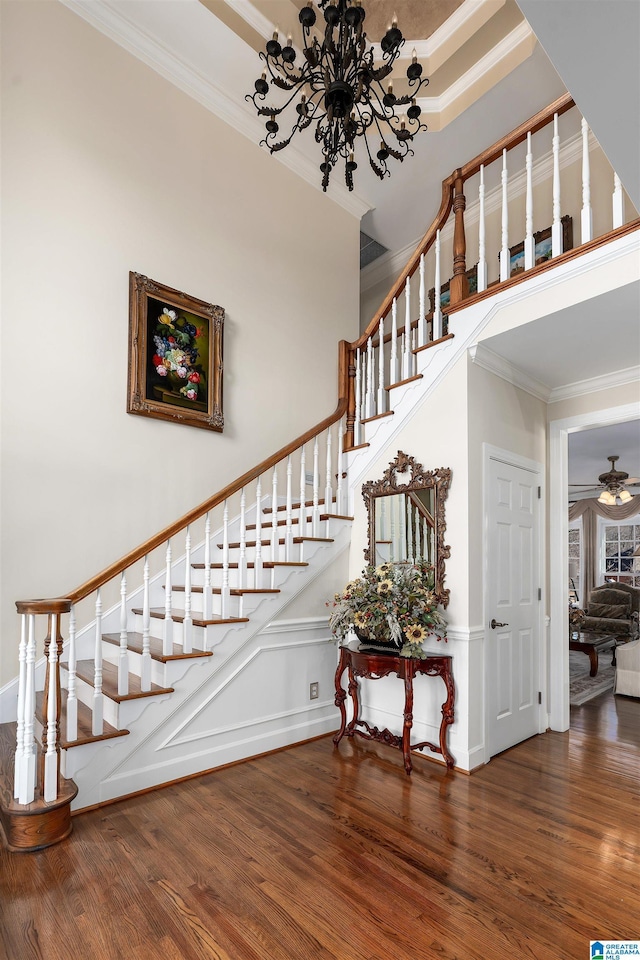 stairs with ceiling fan with notable chandelier, ornamental molding, and hardwood / wood-style floors