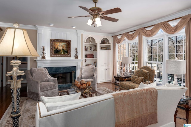 living room featuring hardwood / wood-style floors, a fireplace, built in features, ornamental molding, and ceiling fan