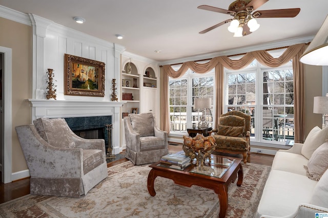 living room featuring wood-type flooring, ceiling fan, a high end fireplace, built in shelves, and ornamental molding