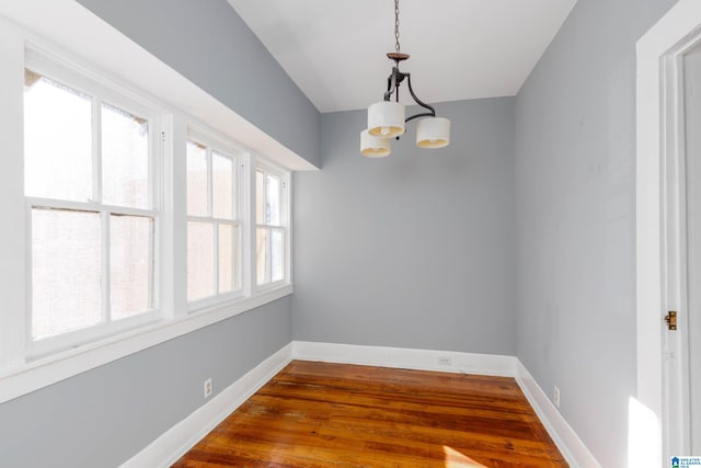 unfurnished dining area with wood-type flooring, a chandelier, and a wealth of natural light