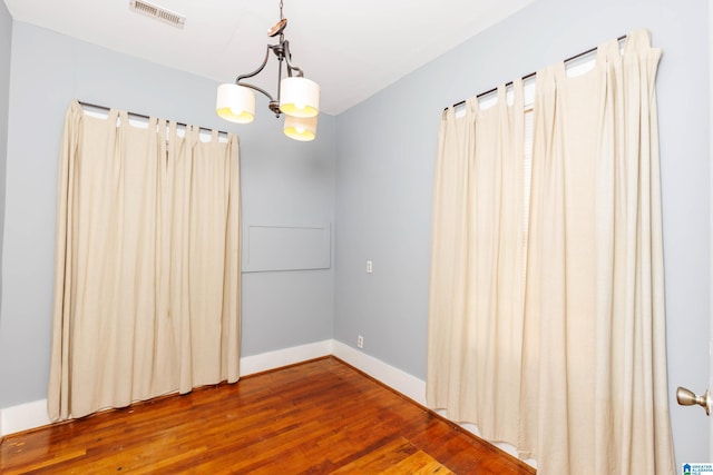 empty room with hardwood / wood-style flooring and a notable chandelier