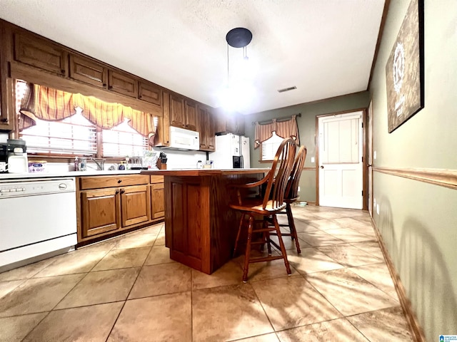 kitchen with sink, light tile patterned flooring, white appliances, a breakfast bar, and a kitchen island