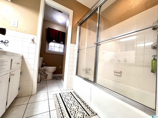 bathroom with tile patterned floors, toilet, a textured ceiling, and combined bath / shower with glass door