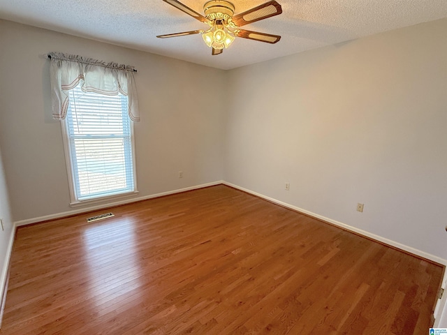 empty room with ceiling fan, wood-type flooring, and a textured ceiling