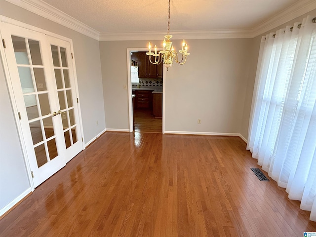 unfurnished dining area with wood-type flooring, ornamental molding, french doors, and an inviting chandelier