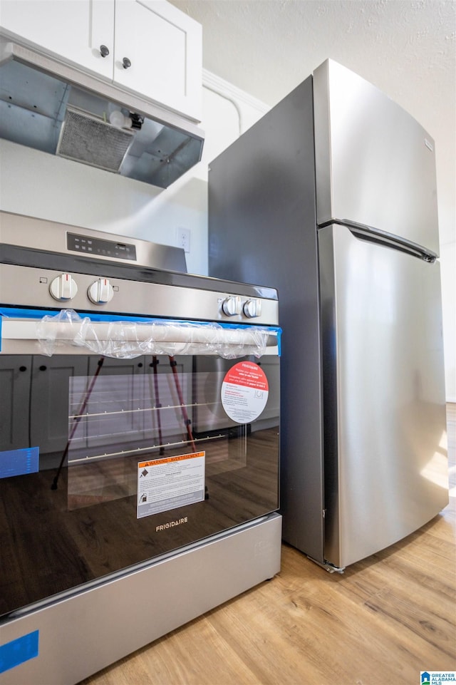 interior details featuring white cabinets, light wood-type flooring, stainless steel fridge, and wall oven