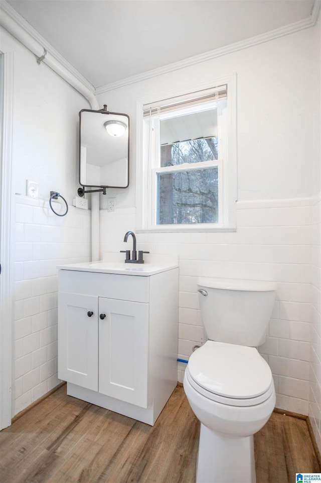 bathroom with tile walls, hardwood / wood-style flooring, toilet, vanity, and ornamental molding