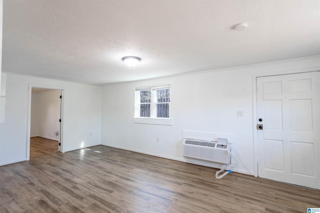 unfurnished room featuring hardwood / wood-style floors, a textured ceiling, and an AC wall unit