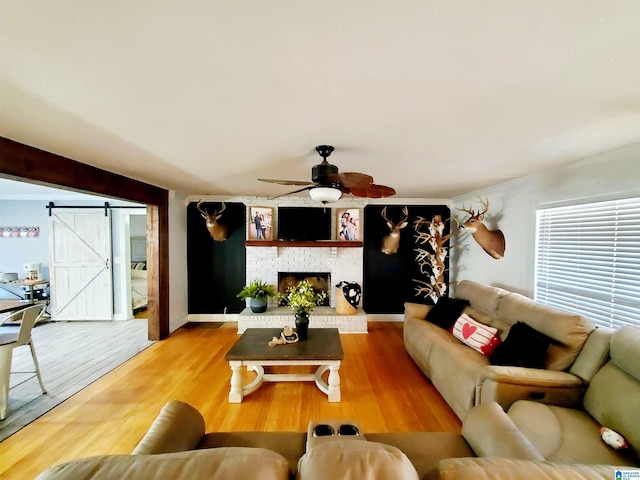 living room with a fireplace, wood-type flooring, ornamental molding, ceiling fan, and a barn door