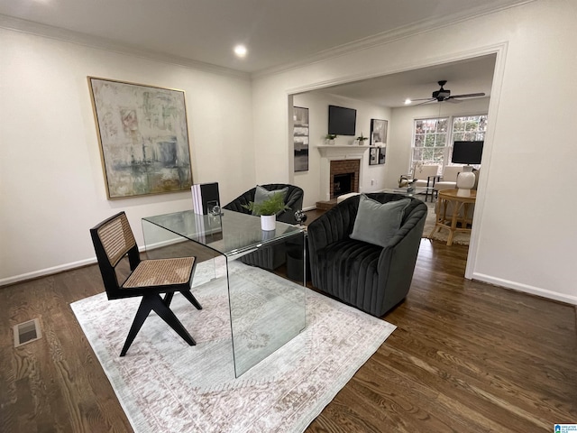 living room featuring dark wood-type flooring, ceiling fan, ornamental molding, and a fireplace