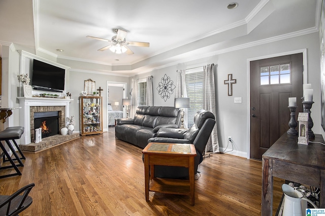 living room featuring a healthy amount of sunlight, hardwood / wood-style flooring, a brick fireplace, and a raised ceiling