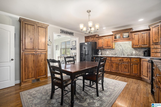 dining area featuring sink, dark wood-type flooring, an inviting chandelier, and ornamental molding