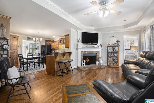 living room with ceiling fan with notable chandelier, dark wood-type flooring, ornamental molding, and a fireplace