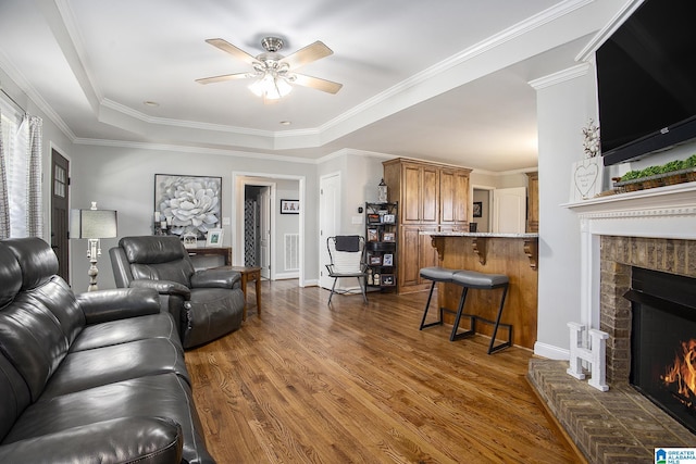 living room with crown molding, ceiling fan, dark hardwood / wood-style flooring, a tray ceiling, and a fireplace