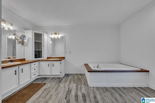 bathroom with a textured ceiling, wood-type flooring, vanity, a washtub, and crown molding