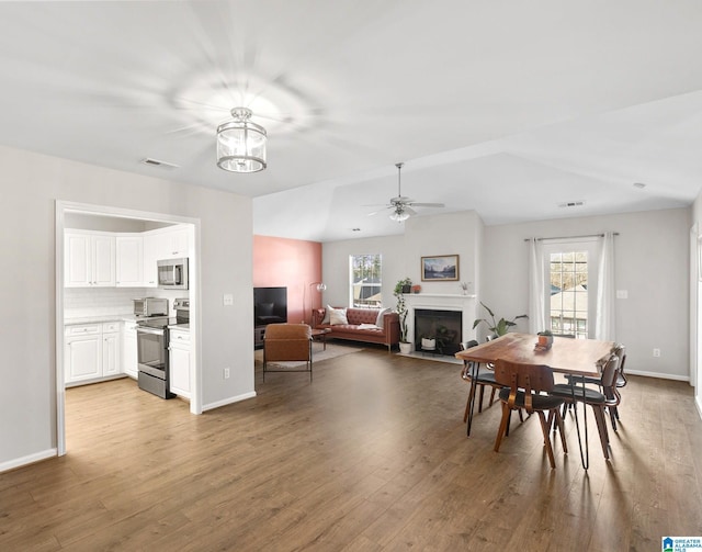 dining room with vaulted ceiling, ceiling fan with notable chandelier, and light hardwood / wood-style floors