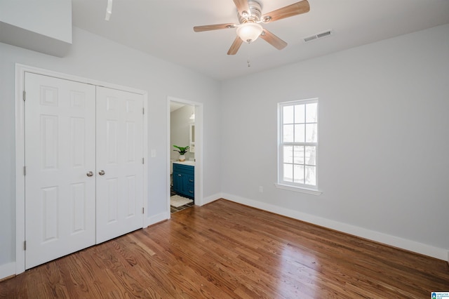 unfurnished bedroom featuring hardwood / wood-style flooring, ensuite bathroom, a closet, and ceiling fan