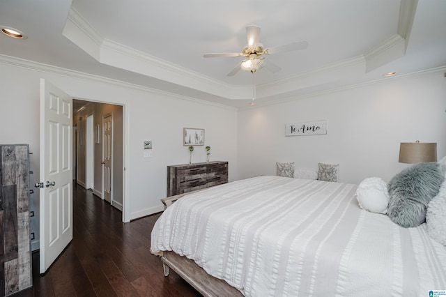 bedroom with crown molding, a tray ceiling, dark wood-type flooring, and ceiling fan