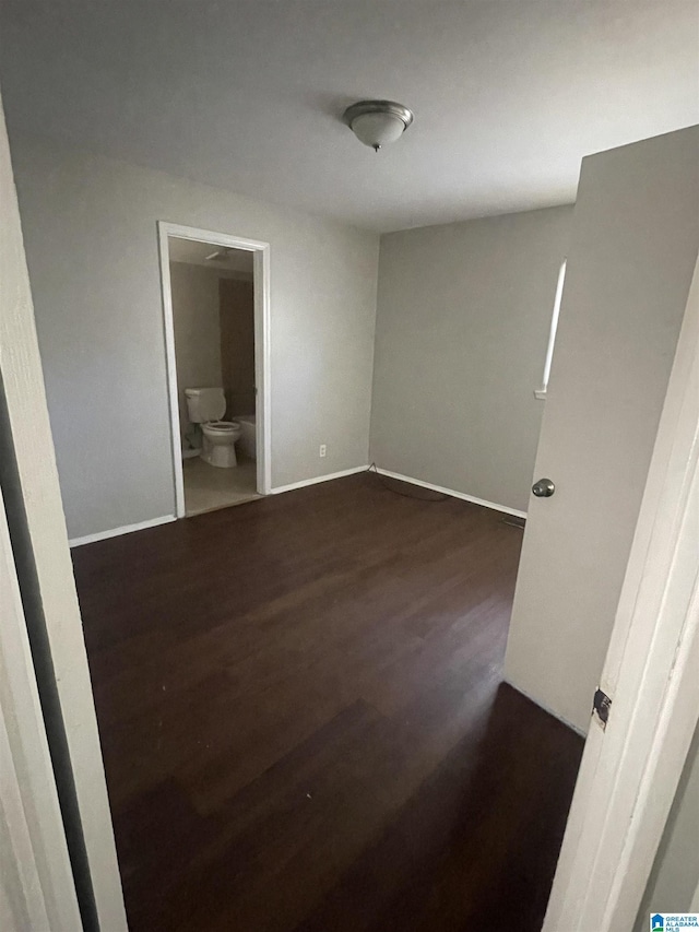 unfurnished bedroom with baseboards, dark wood finished floors, and connected bathroom