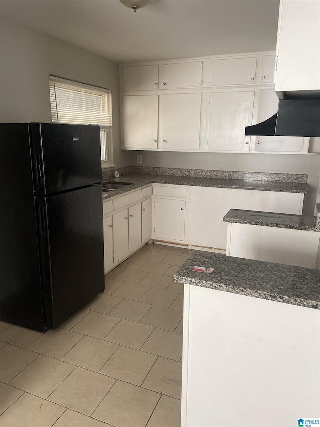 kitchen with light tile patterned floors, dark countertops, freestanding refrigerator, white cabinets, and exhaust hood