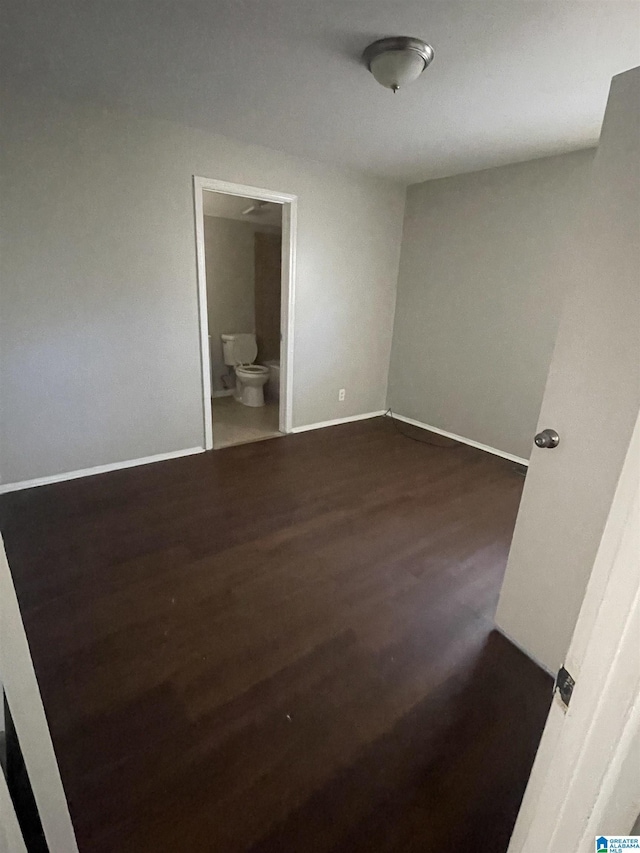 unfurnished bedroom featuring ensuite bathroom, dark wood finished floors, and baseboards