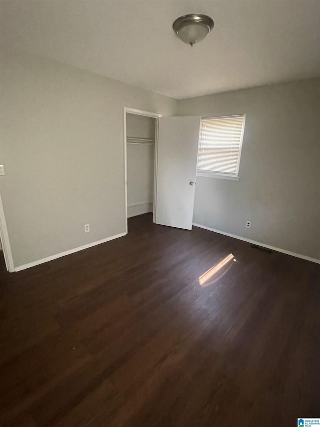 unfurnished bedroom with dark wood-style flooring, a closet, and baseboards