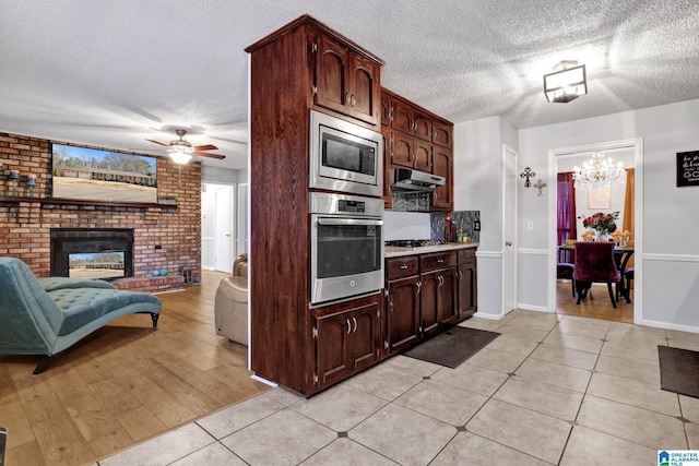 kitchen featuring dark brown cabinets, ceiling fan, light tile patterned floors, a brick fireplace, and stainless steel appliances