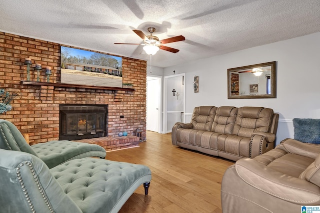 living room with light hardwood / wood-style floors, a textured ceiling, ceiling fan, and a fireplace