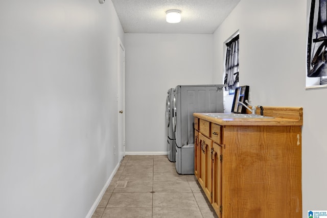 laundry room with a textured ceiling, light tile patterned floors, sink, washer and dryer, and cabinets