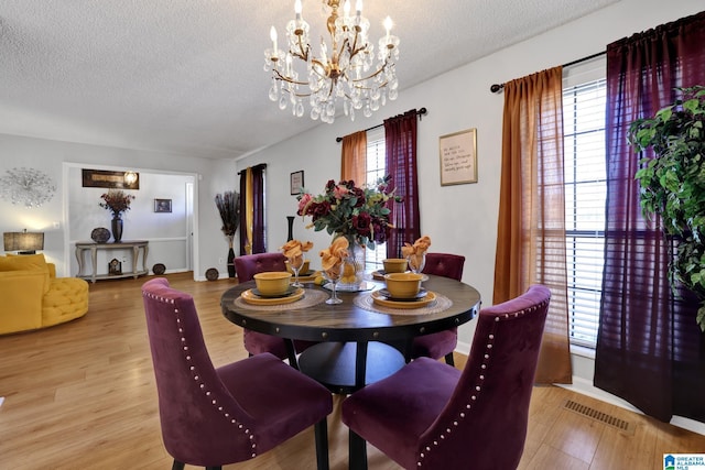 dining room with a textured ceiling, light hardwood / wood-style flooring, and a notable chandelier