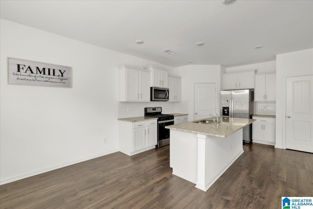 kitchen with appliances with stainless steel finishes, sink, white cabinets, light stone countertops, and a center island with sink