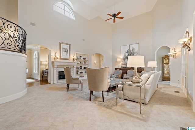 living room featuring built in features, ceiling fan, a high ceiling, and a fireplace