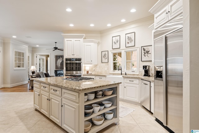 kitchen with light stone countertops, appliances with stainless steel finishes, a kitchen island, white cabinetry, and sink