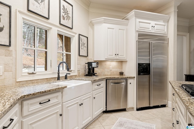 kitchen featuring appliances with stainless steel finishes, white cabinetry, light tile patterned floors, sink, and light stone counters