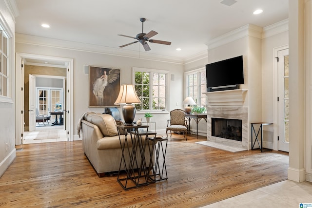 living room with a premium fireplace, light wood-type flooring, ceiling fan, and ornamental molding