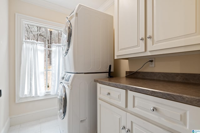 clothes washing area with cabinets, light tile patterned floors, ornamental molding, and stacked washer and dryer