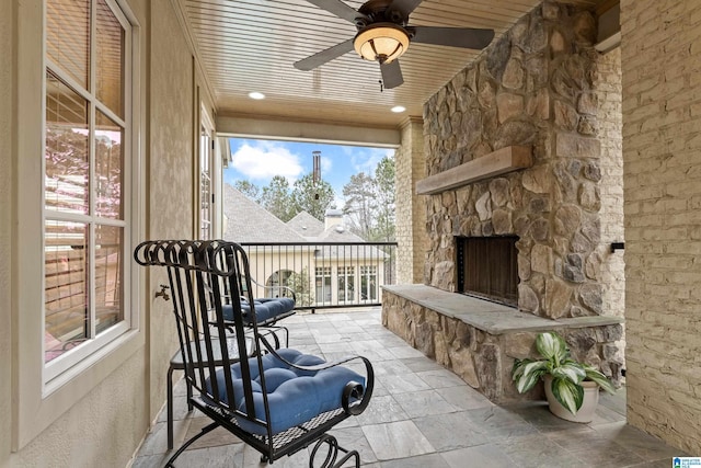 sunroom with an outdoor stone fireplace, ceiling fan, and wood ceiling