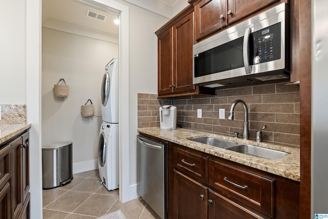 kitchen with crown molding, sink, light stone counters, stacked washer / drying machine, and stainless steel appliances