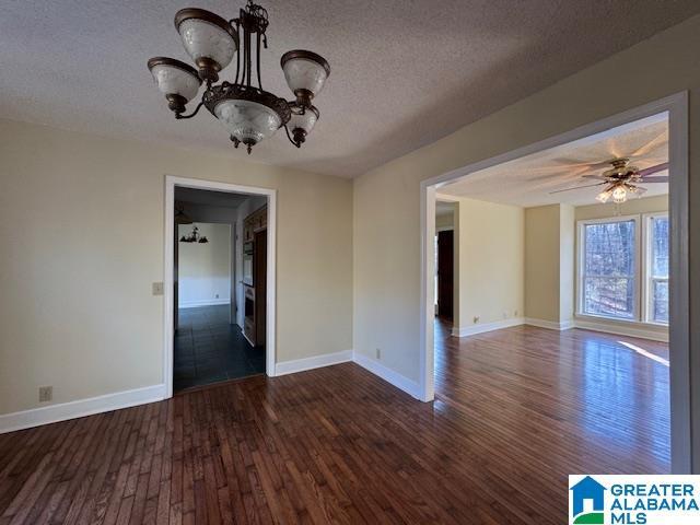 unfurnished room with ceiling fan with notable chandelier, a textured ceiling, and dark hardwood / wood-style flooring